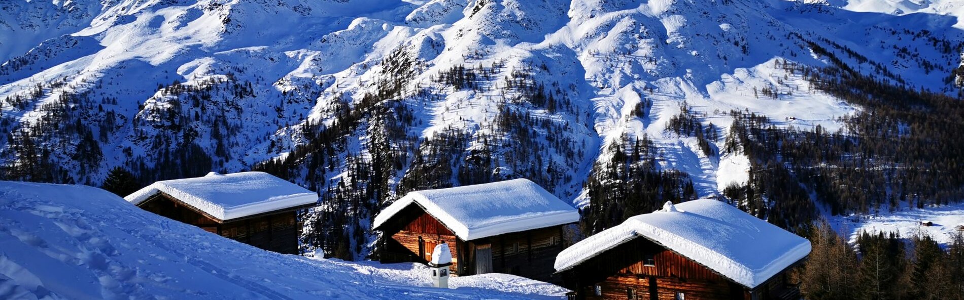 drei verschneite Holzhütte mit einer Bergpanorama im Hintergrund