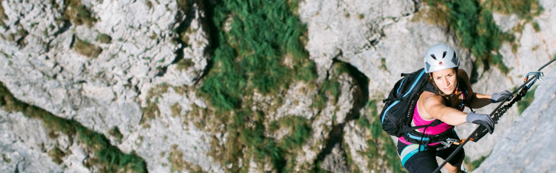 Frau klettert entlang eines Drahtseiles. Im Hintergrund sieht man hellgrauen Fels.