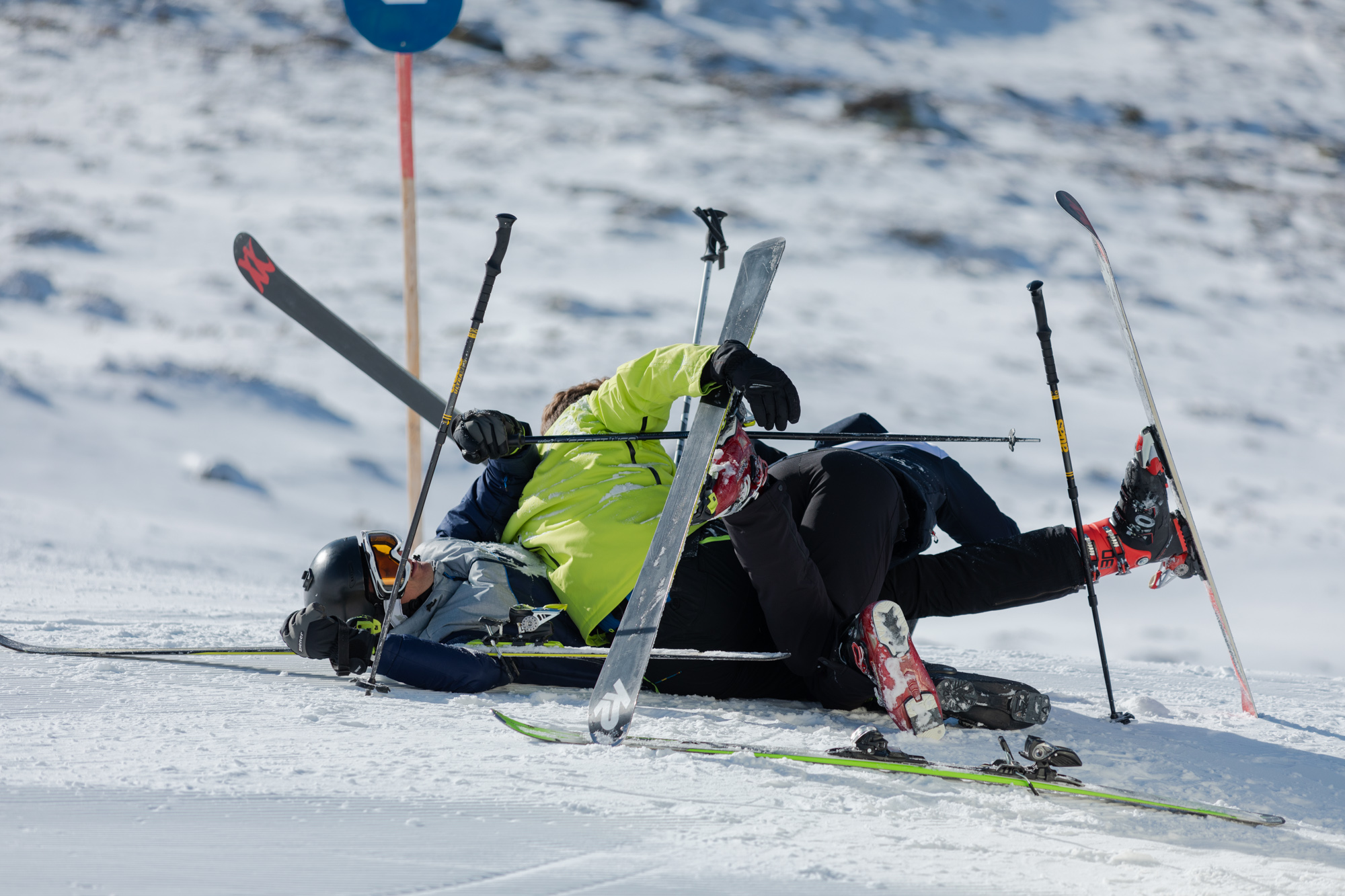 Three skiers lie wildly knotted in a heap on ski slope.