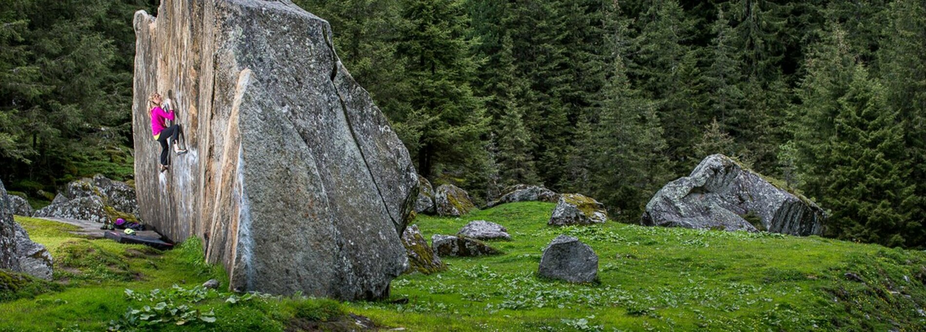 Large boulder on a meadow on which a young woman climbs. 