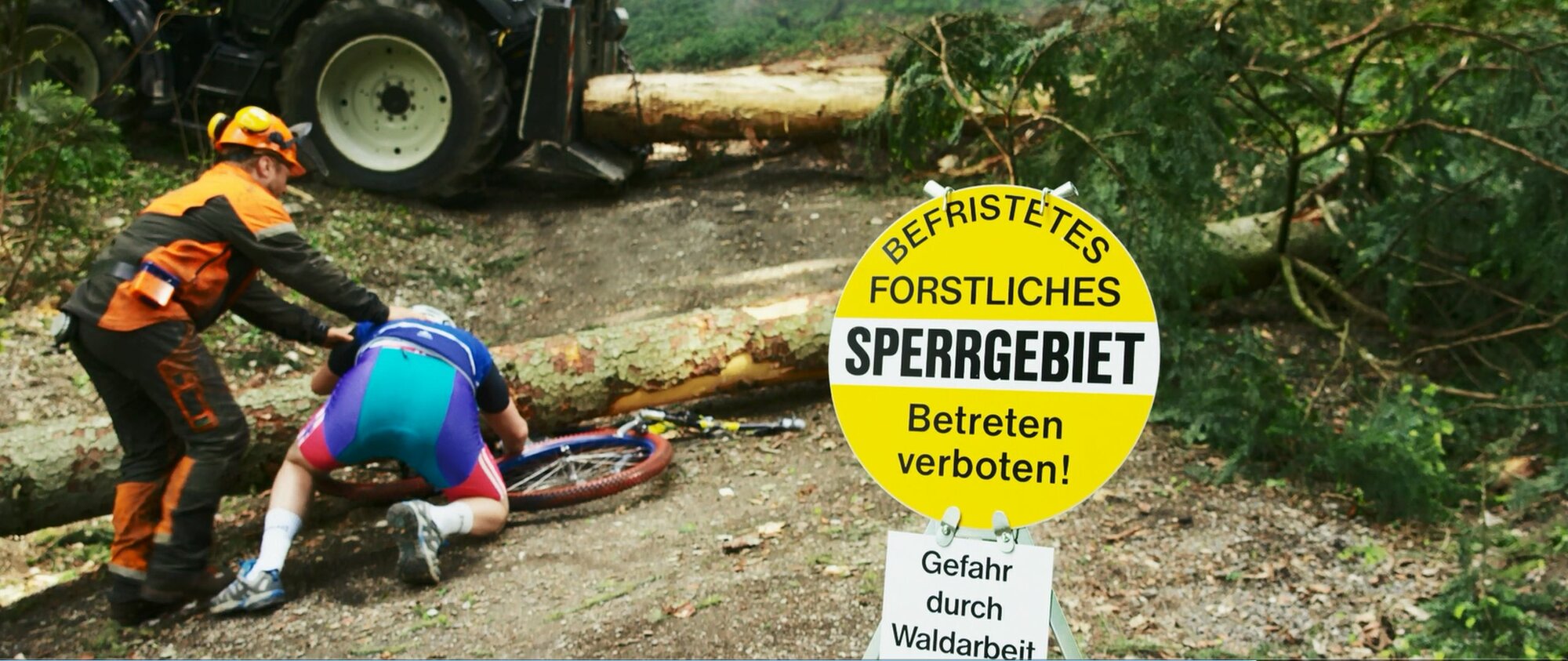 Ein Forstliches Sperrgebietschild. Im Hintergrund eine Forstarbeiter der sich über einen Mountainbiker beugt. Sein Bike liegt unter einem Baumstamm.