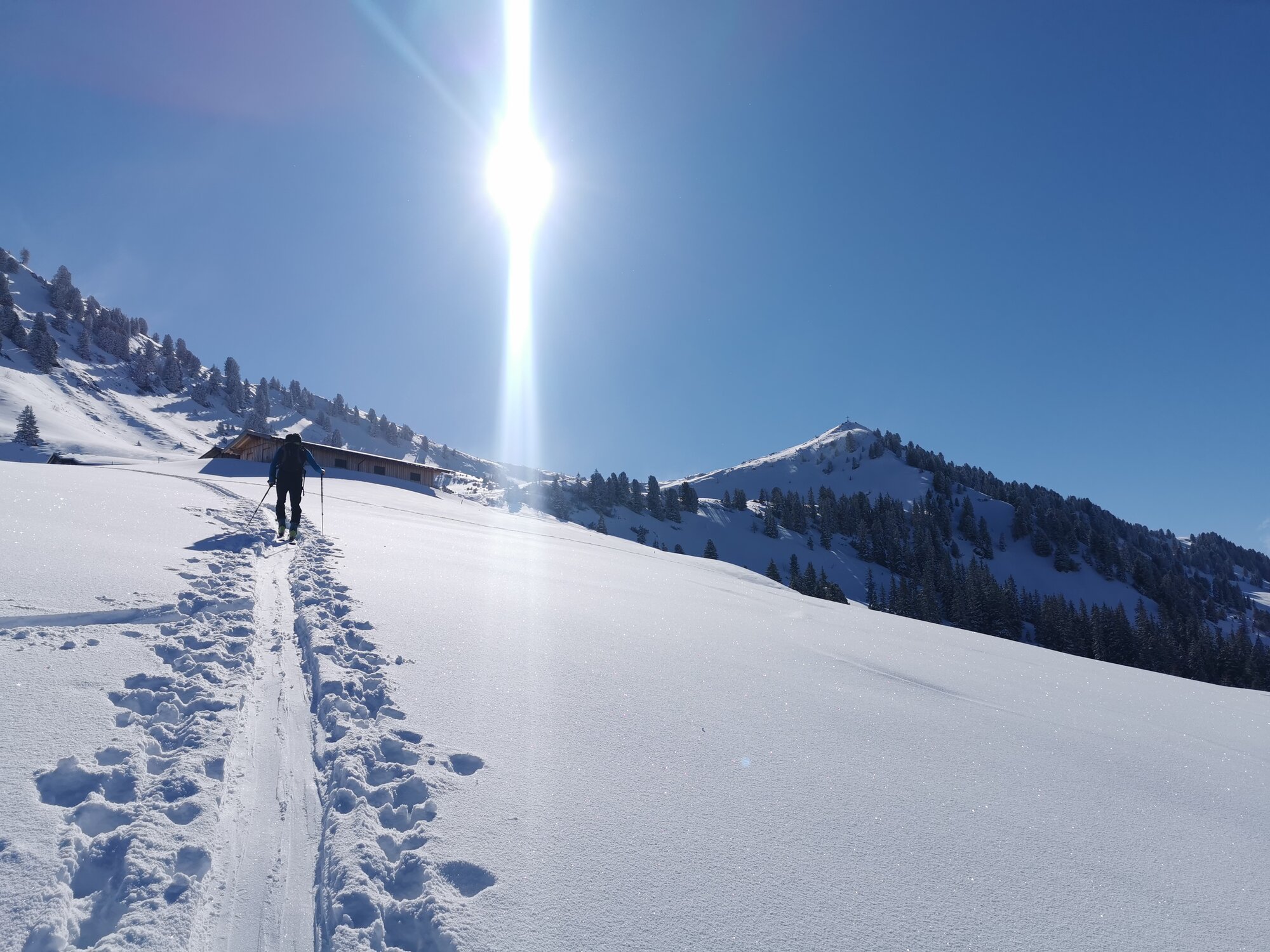 Tourengeher folgt einer Spur durch einen Tiefschneehang Richtung Gipfel bei strahlendem Sonnenschein. © C. Silberberger, Wildschönau Tourismus