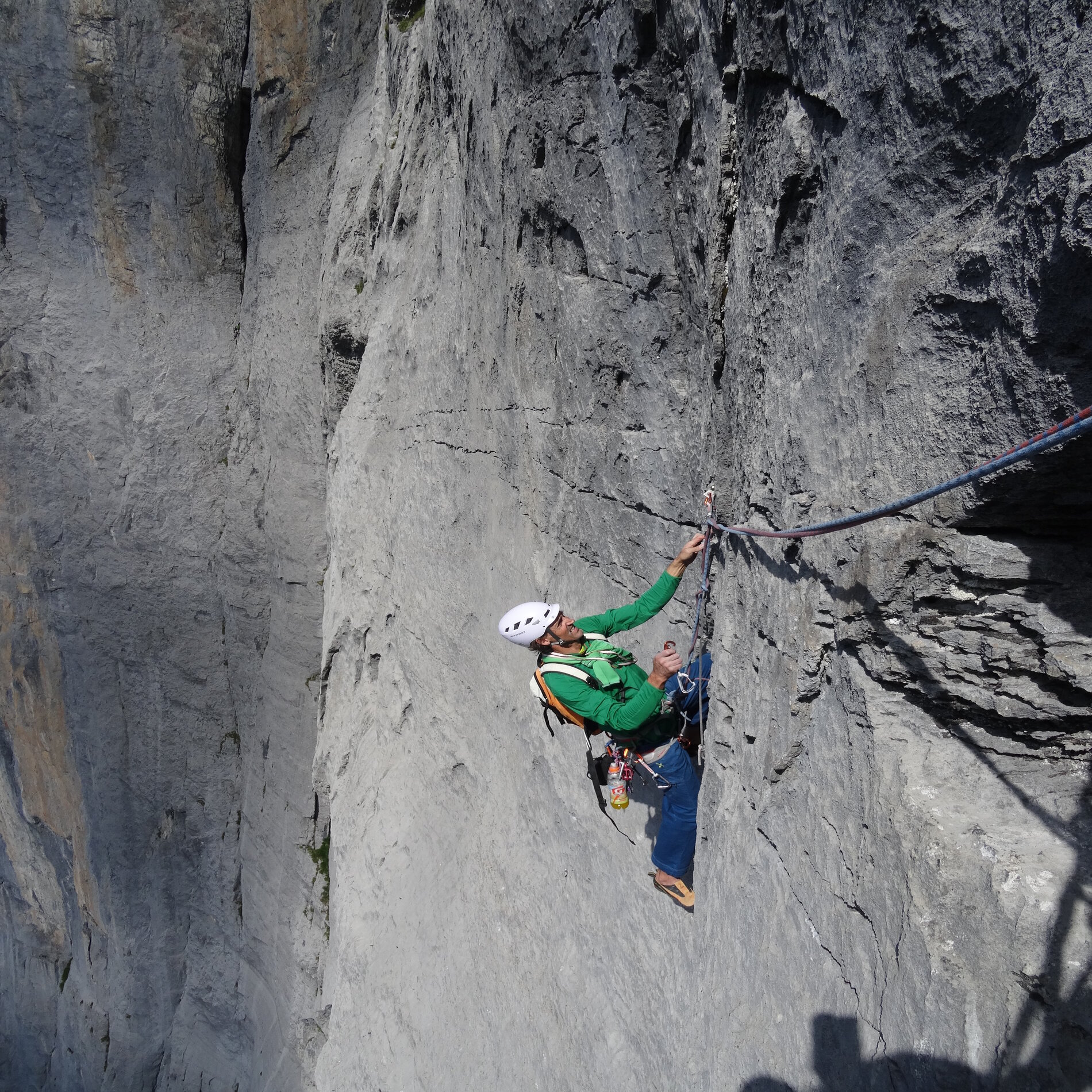 Ein Kletterer mit Helm klettert eine hellgraue Kalkfelswand hinauf.