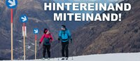 A woman and a man walk side by side up the slope with touring skis.