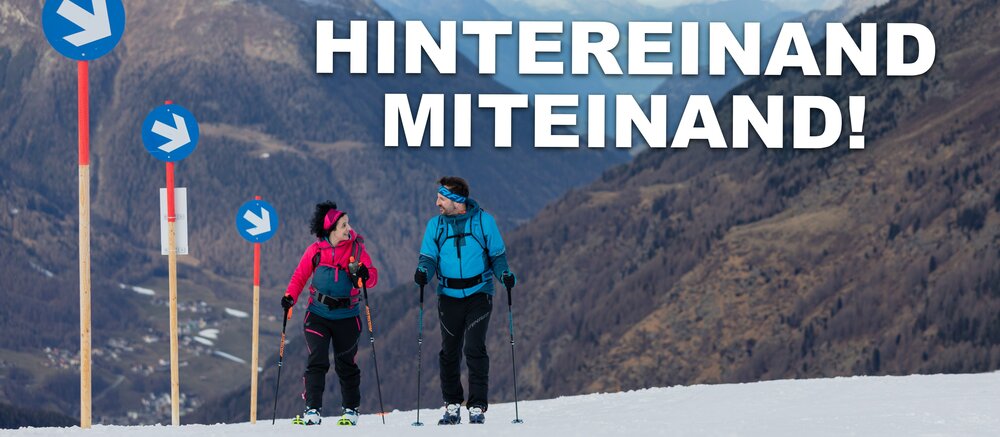 A woman and a man walk side by side up the slope with touring skis.