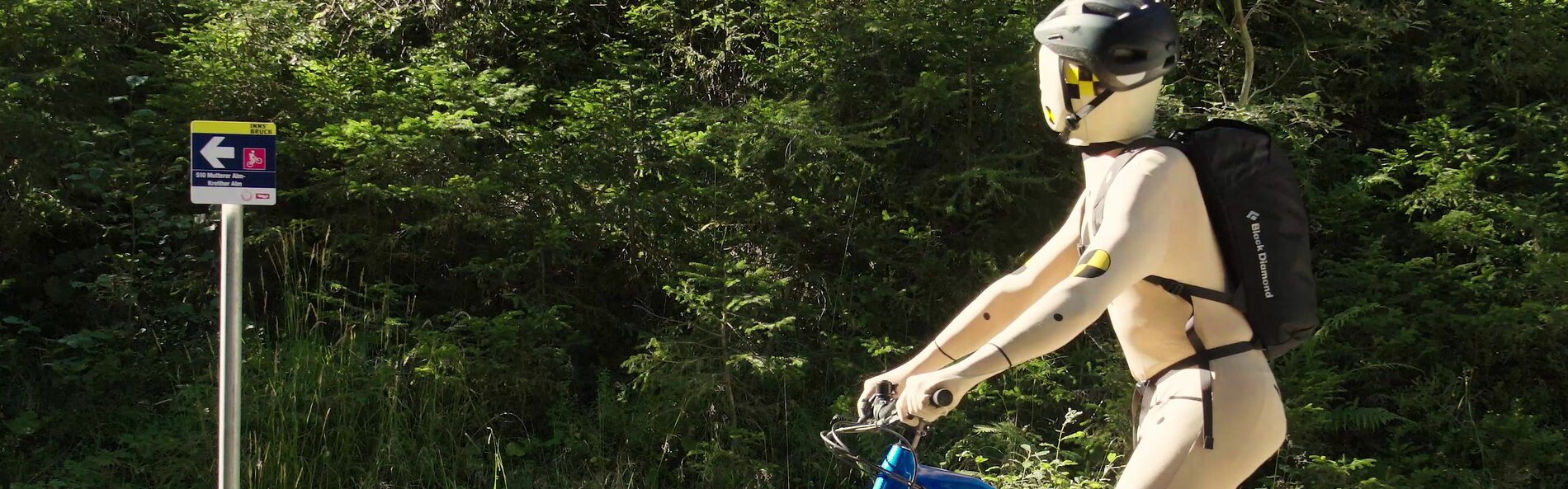 Doll dressed as mountain biker looks at a sign