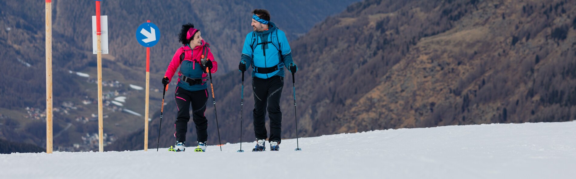 A woman and a man walk side by side up the slope with touring skis.