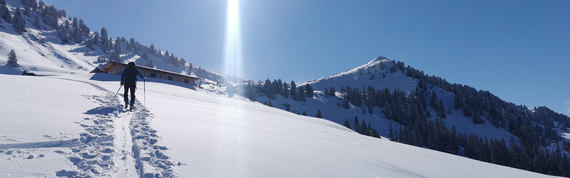 Tourengeher folgt einer Spur durch einen Tiefschneehang Richtung Gipfel bei strahlendem Sonnenschein. © C. Silberberger, Wildschönau Tourismus