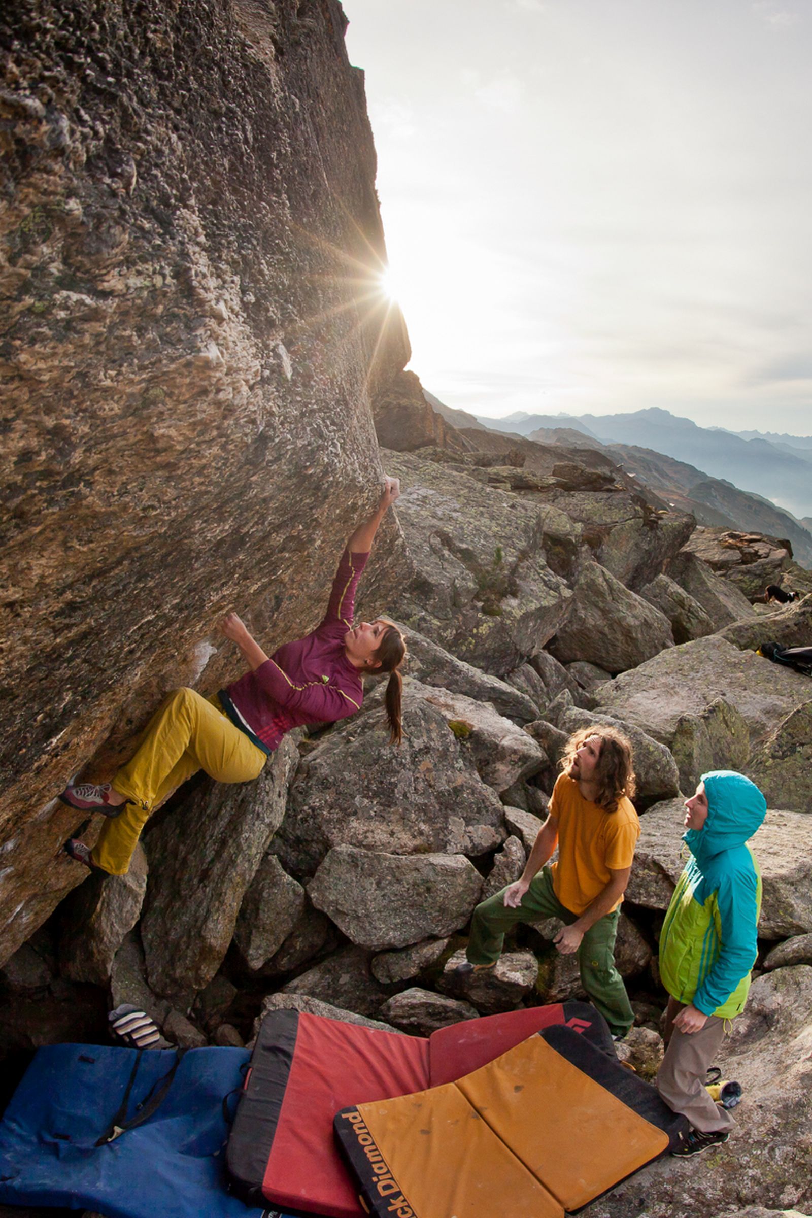 A young woman climbs a boulder. 