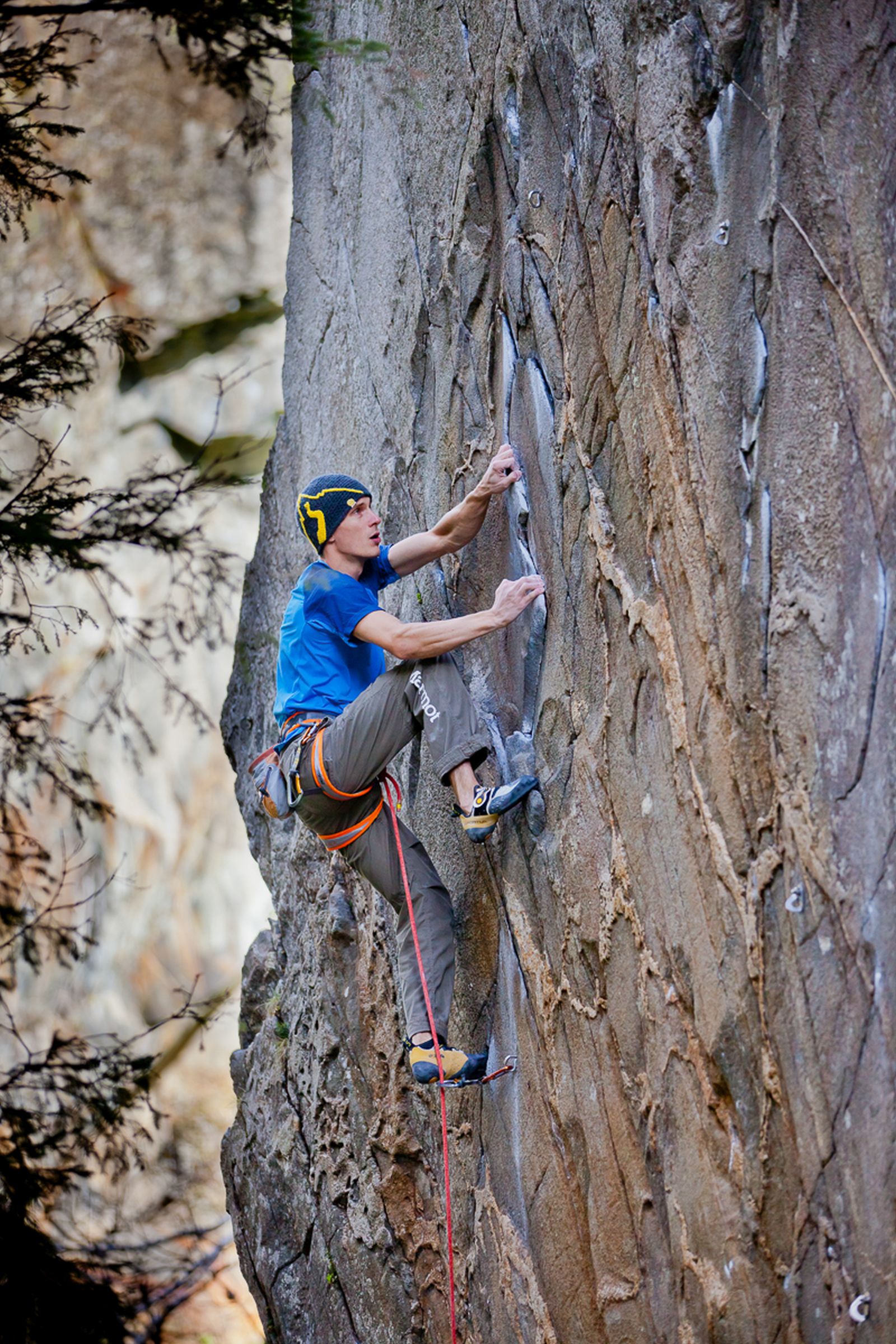 Man climbing up a rock wall; secured with rope. 